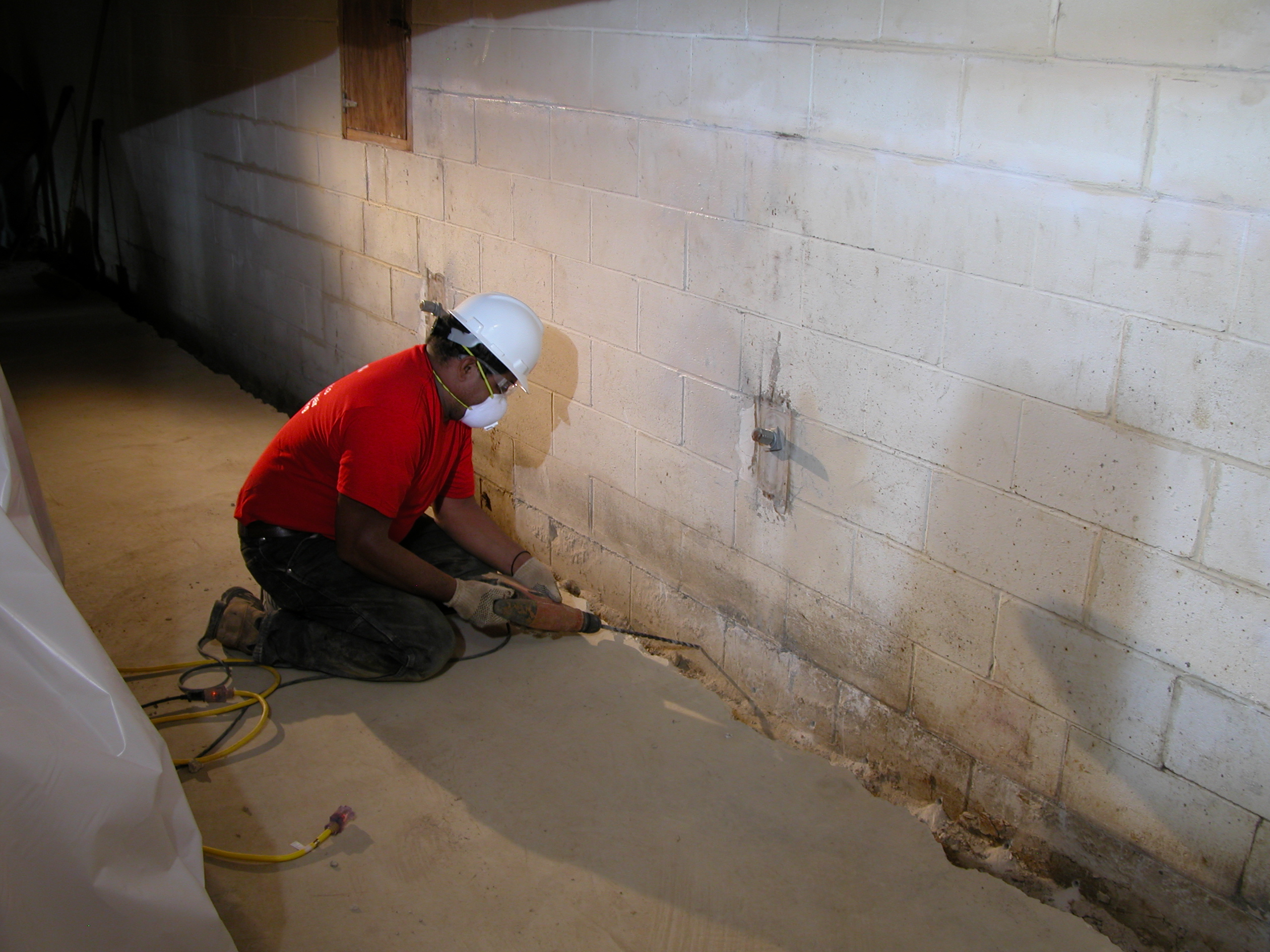 Basement specialist using precision drilling to prepare for advanced waterproofing solutions and moisture prevention in lower-level home environment Basement specialist using precision drilling to prepare for advanced waterproofing solutions and moisture prevention in lower-level home environment
