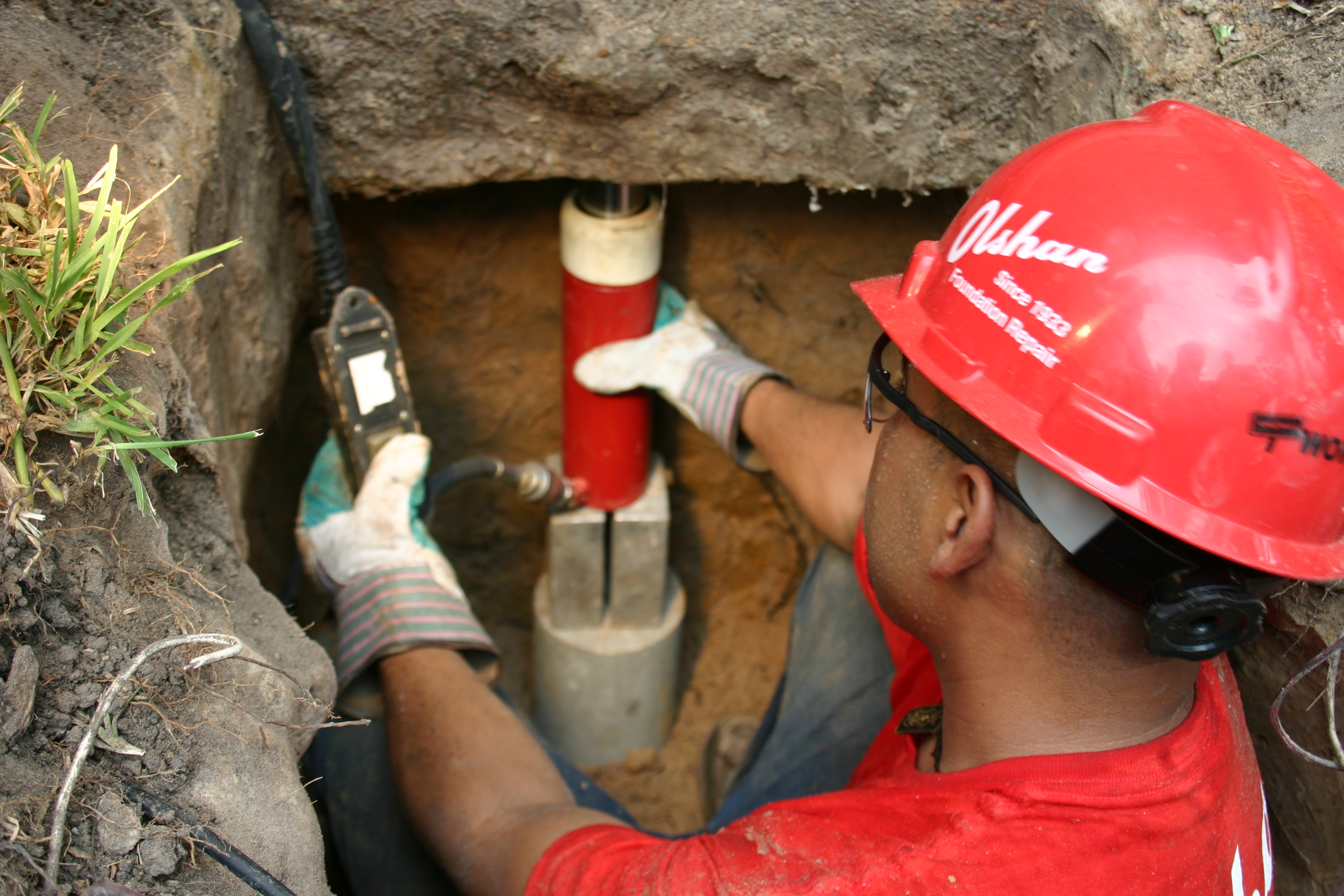 Skilled technician operating hydraulic equipment for efficient steel pier installation under home foundations. Skilled technician operating hydraulic equipment for efficient steel pier installation under home foundations.