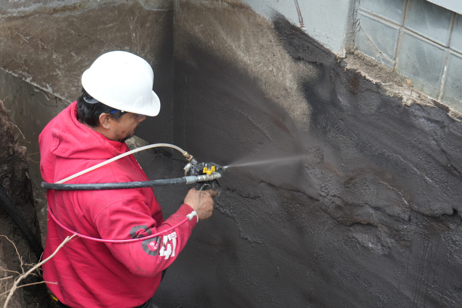 Olshan Certified Structural Technician spray applying WetSuit rubberized membrane to an excavated exterior basement wall