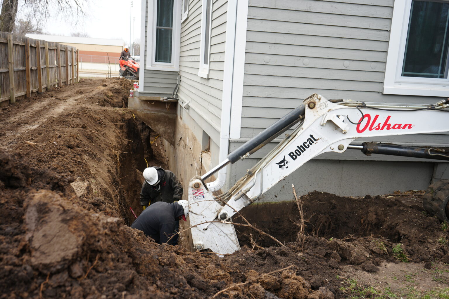 Olshan crew excavating along an exterior basement wall with a compact excavator