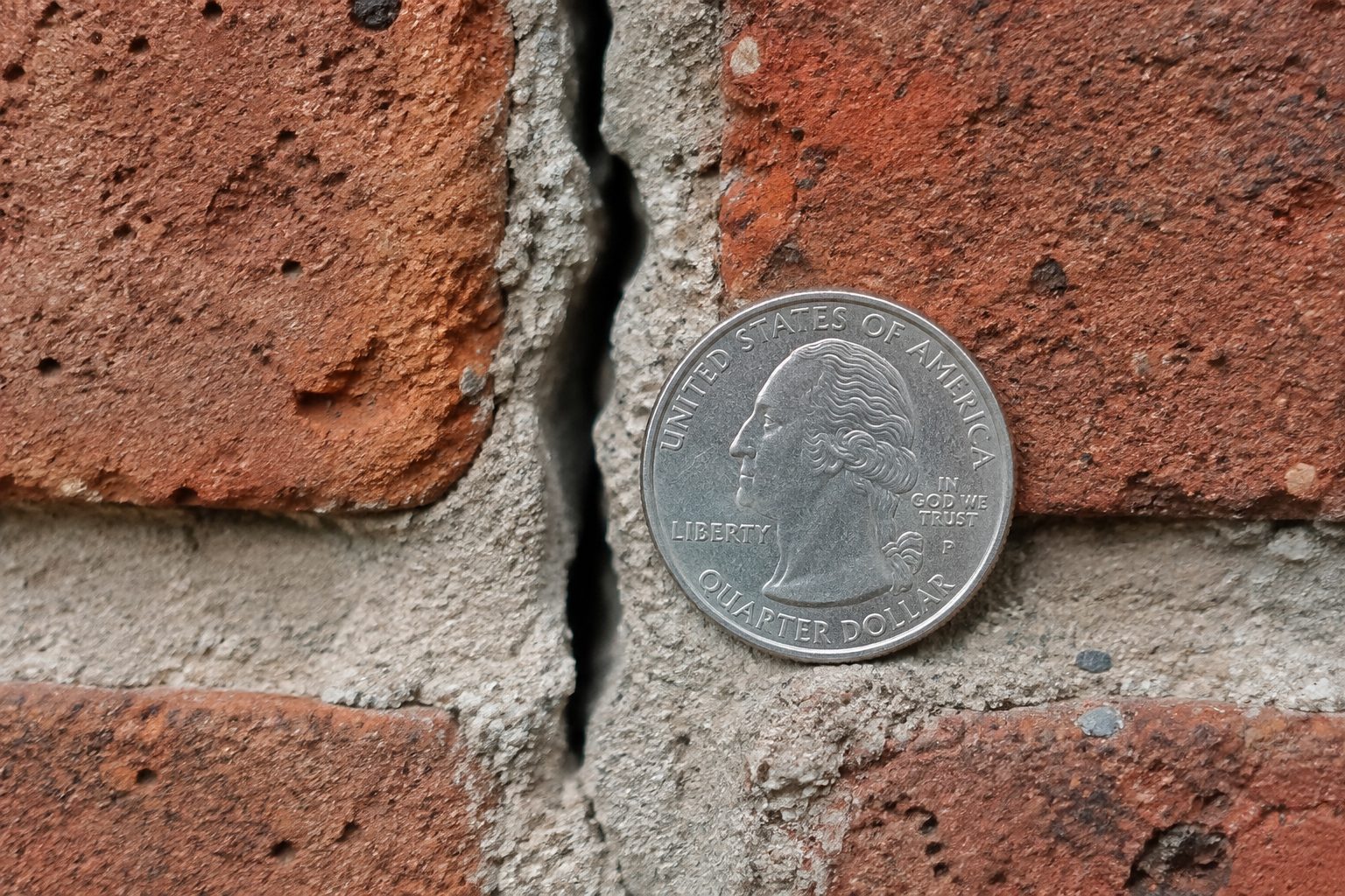 Quarter placed beside a mortar crack in brick to show crack width for scale