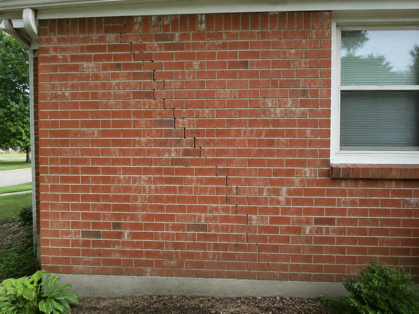 Stair-step crack climbing through mortar joints in a brick exterior wall